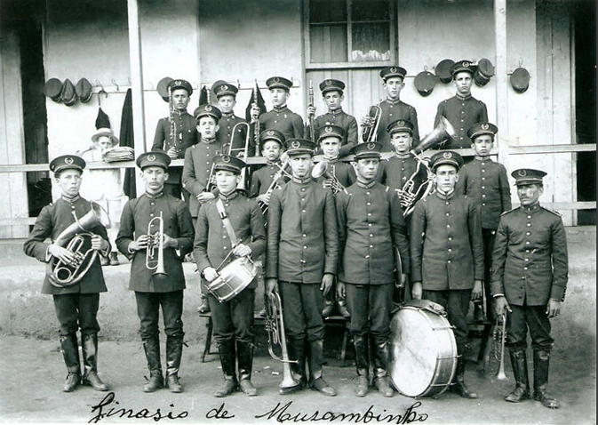 A banda marcial do Ginásio de Muzambinho. Repare que atrás dos talentosos músicos, na parede, há alguns ganchos em que eles penduravam jaquetas e quepes. Há também um menininho, à esquerda, de chapéu panamá, observando a banda e, provavelmente, morrendo de vontade de participar dela