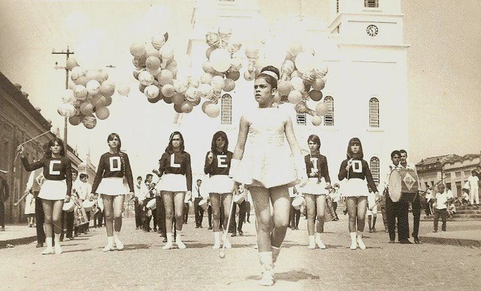 Da esquerda para a direita, as meninas representando cada letra da palavra COLÉGIO, são: Scarlett Abrahão, Joelita Senedese, Leda Macedo, Maria Helena Carli, garota não identificada, Betinha Machado, Ana Rachel (prima de Joelita Senedese) e Betinha Machado. Bragão (com instrumento) e Waltinho Cipriani. À frente vemos a baliza, quem seria a bela moça? Foto: Reprodução Facebook 